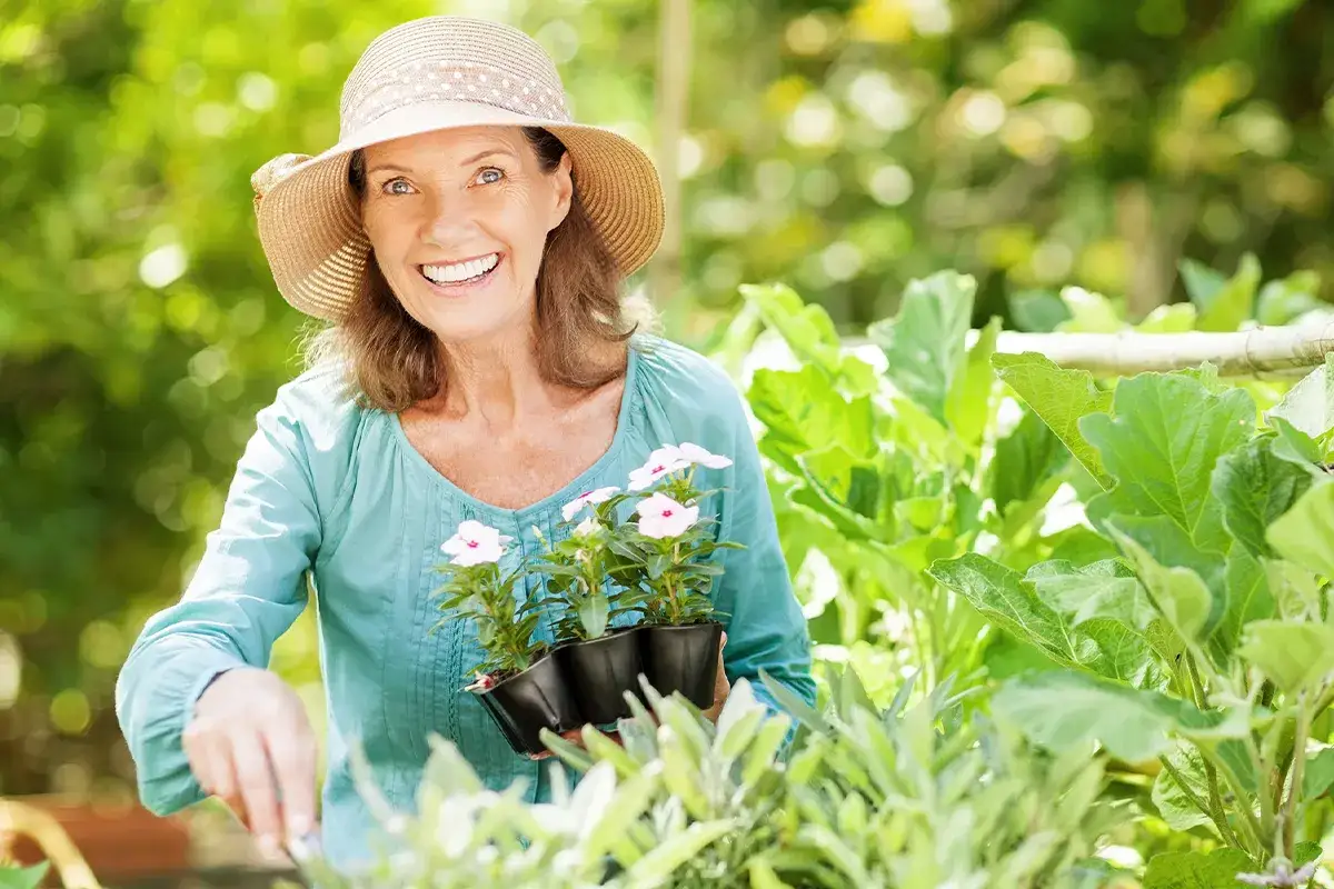 Frontalaufnahme einer ältere weiblichen Person in der Natur mit Pflanzblumen in der Hand stehend