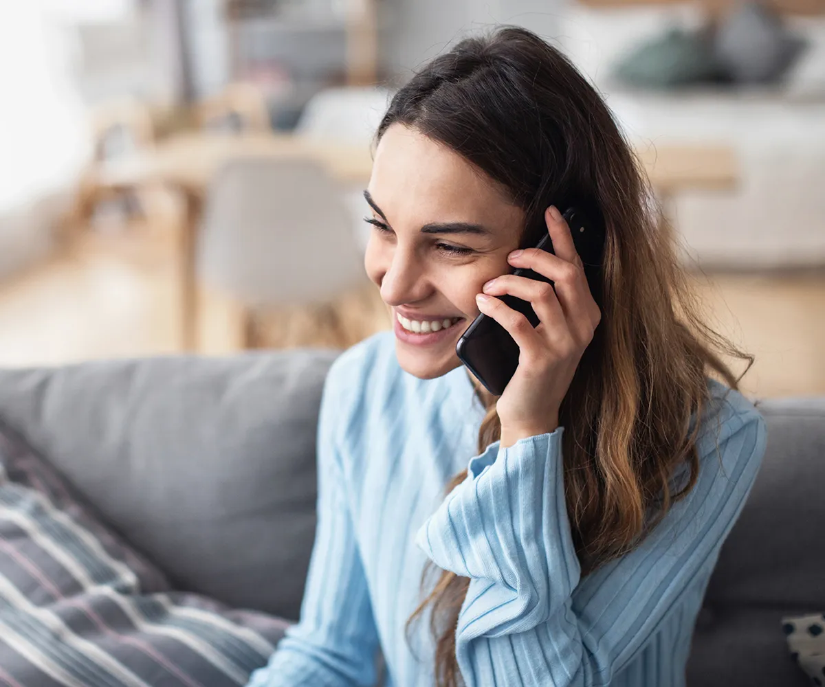 Eine weibliche Person mit Handy am Ohr auf einer Couch sitzend
